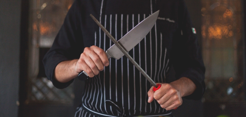 chef sharpening a knife while standing behind a kitchen counter